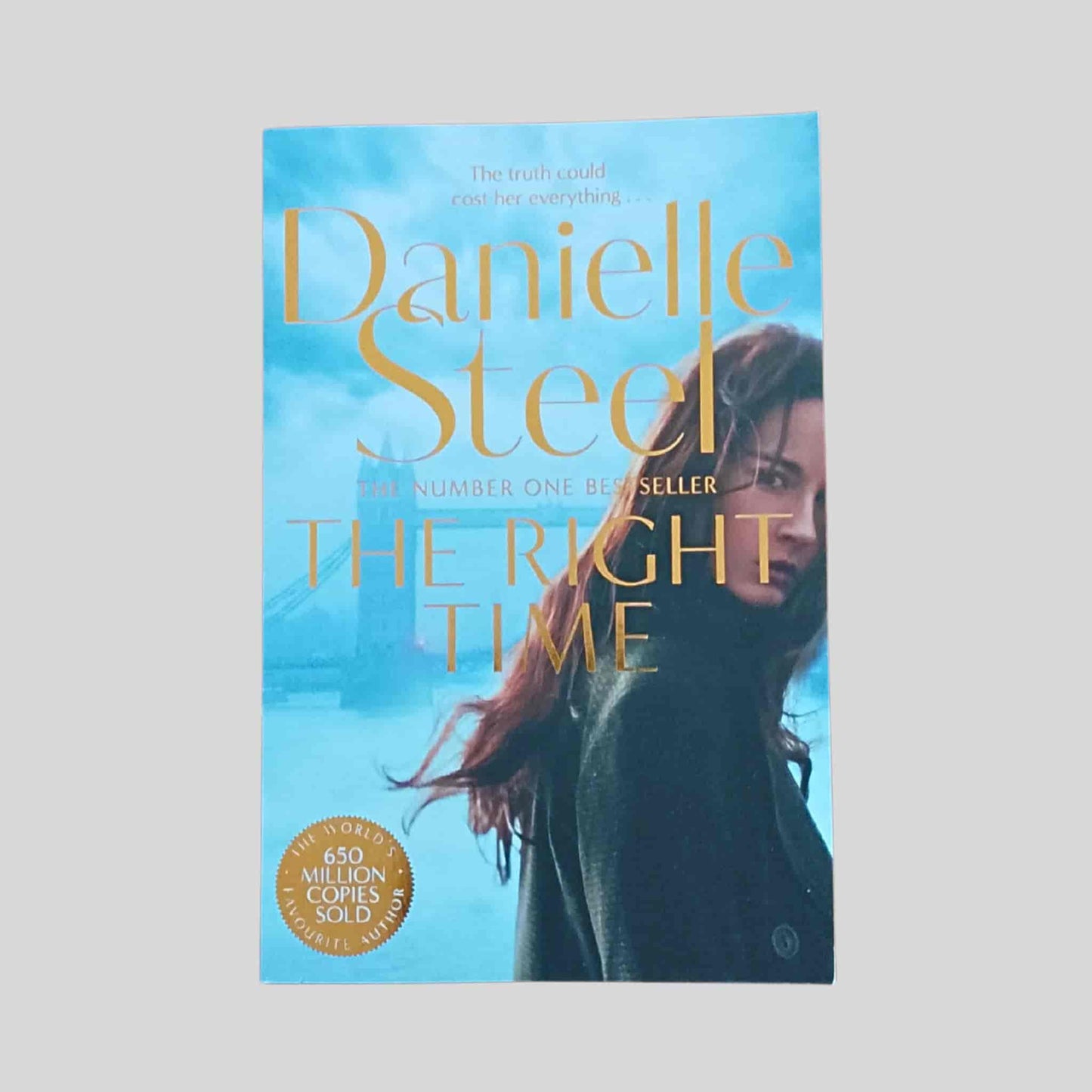 Paperback book cover of The Right Time by Danielle Steel, showing a woman in a dark coat looking over her shoulder against a blue cityscape background