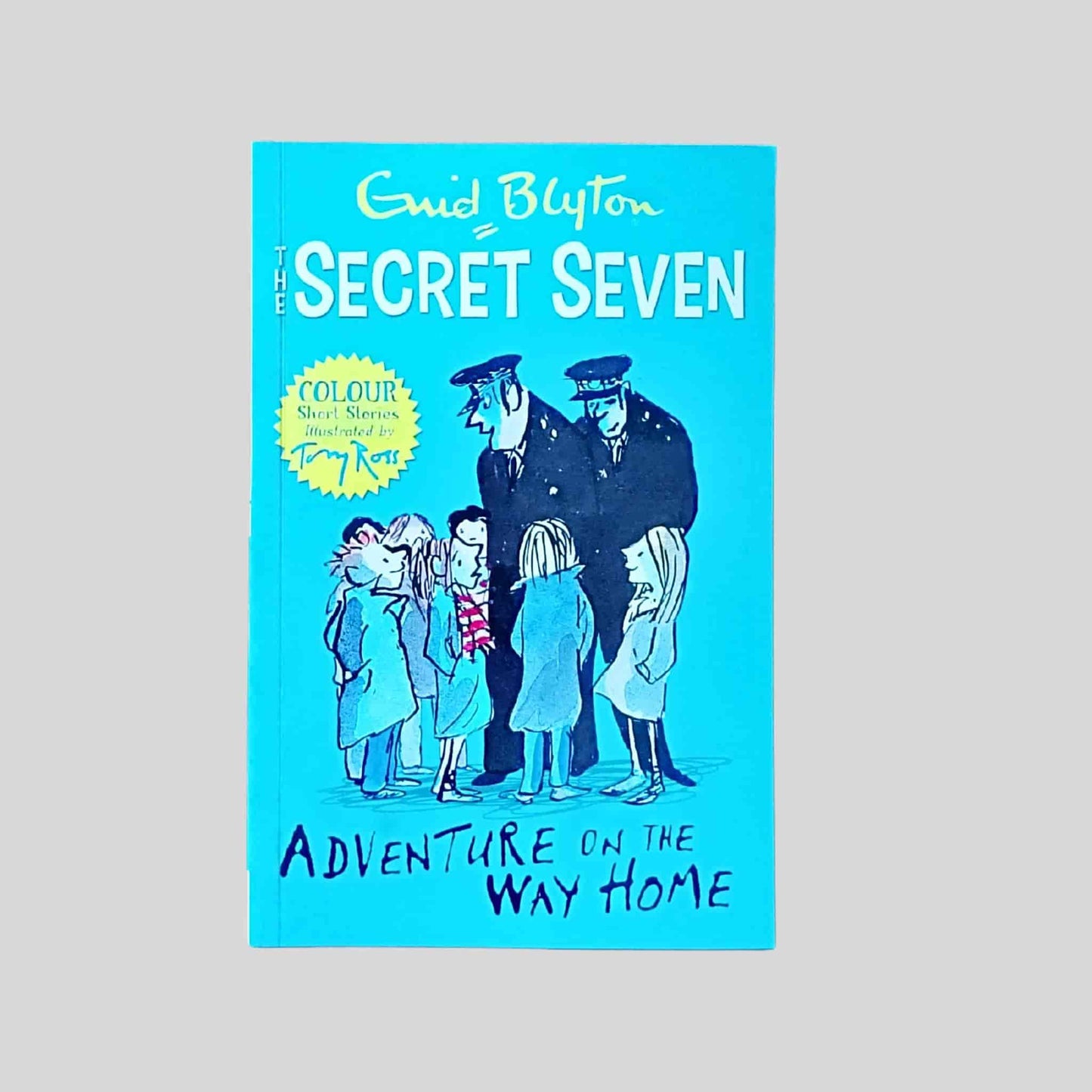 The front cover of the book called The Secret Seven Adventure on the Way Home by Enid Blyton showing the Secret Seven standing with two policemen on a blue illustrated cover