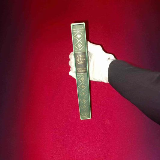 Collectible leather-bound edition of A Tale of Two Cities by Charles Dickens held against a red fabric background