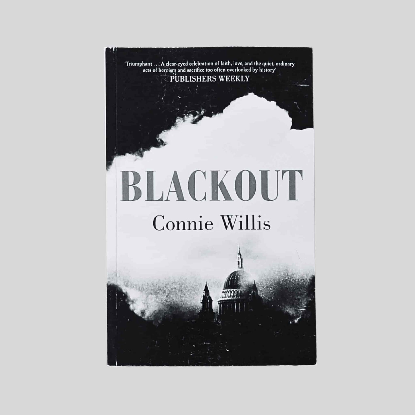 A book cover of Blackout by Connie Willis, showing a black and white illustration of a wartime London skyline with St Paul’s Cathedral emerging through smoke and shadow