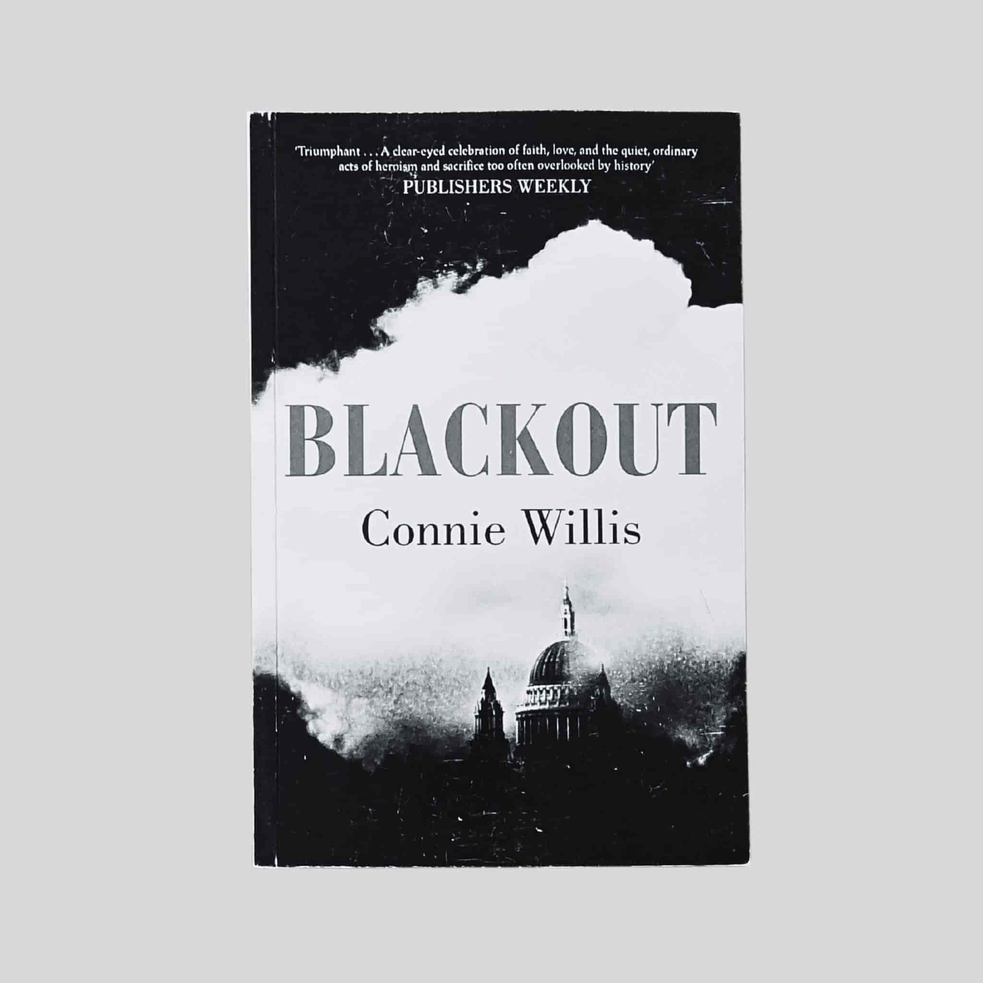 A book cover of Blackout by Connie Willis, showing a black and white illustration of a wartime London skyline with St Paul’s Cathedral emerging through smoke and shadow