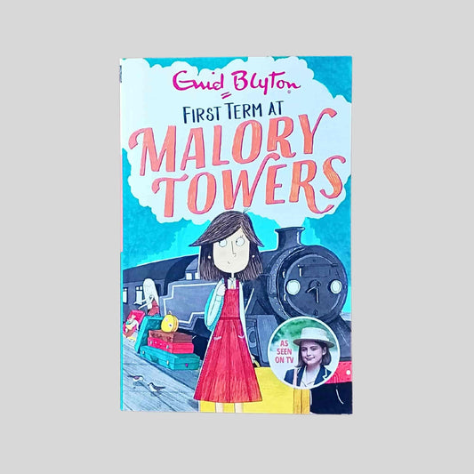 The front cover of the book called First Term at Malory Towers by Enid Blyton showing an illustration of a schoolgirl standing on a railway platform beside a steam train