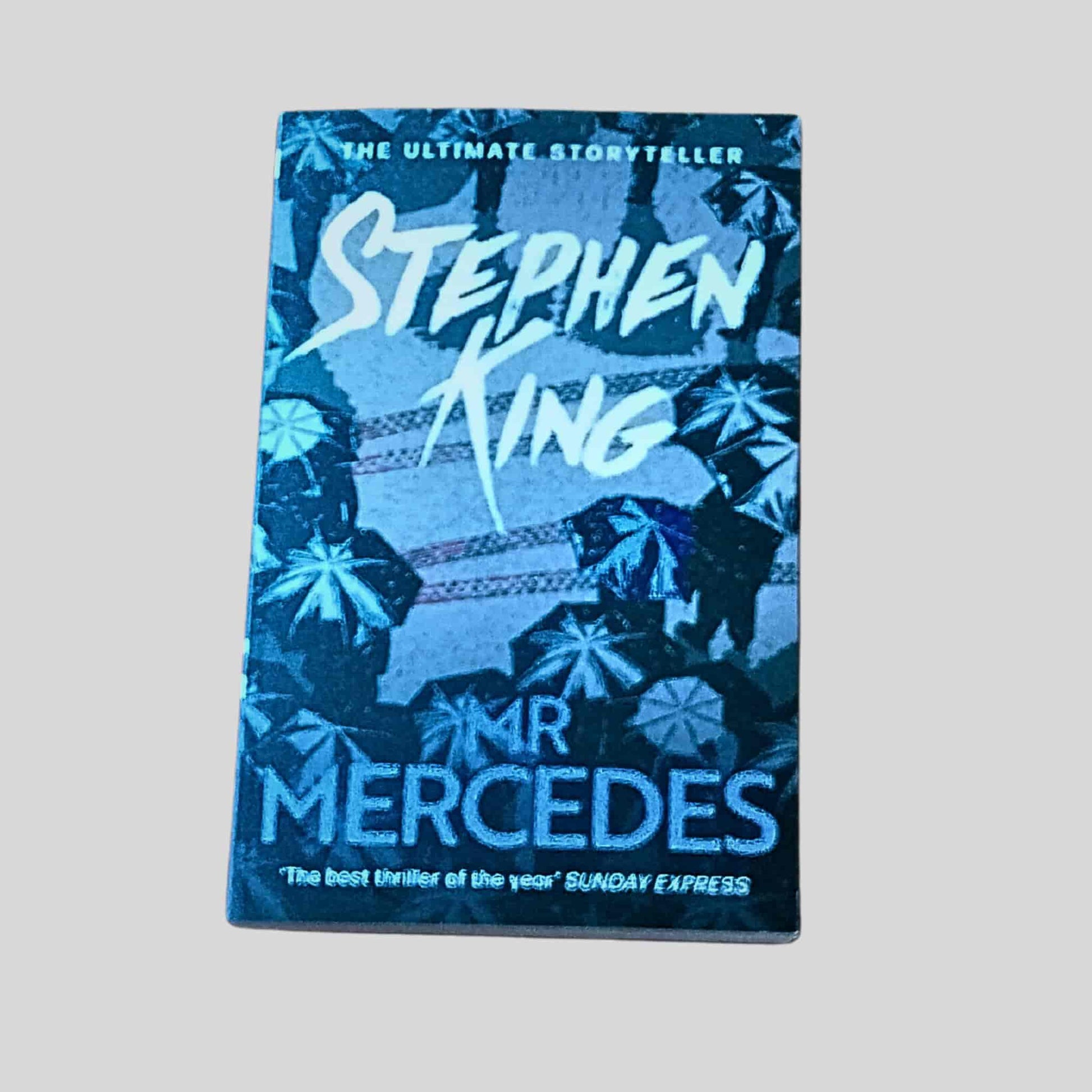The front cover of Mr Mercedes by Stephen King in paperback, showing a dark blue design with umbrellas and the title in bold lettering
