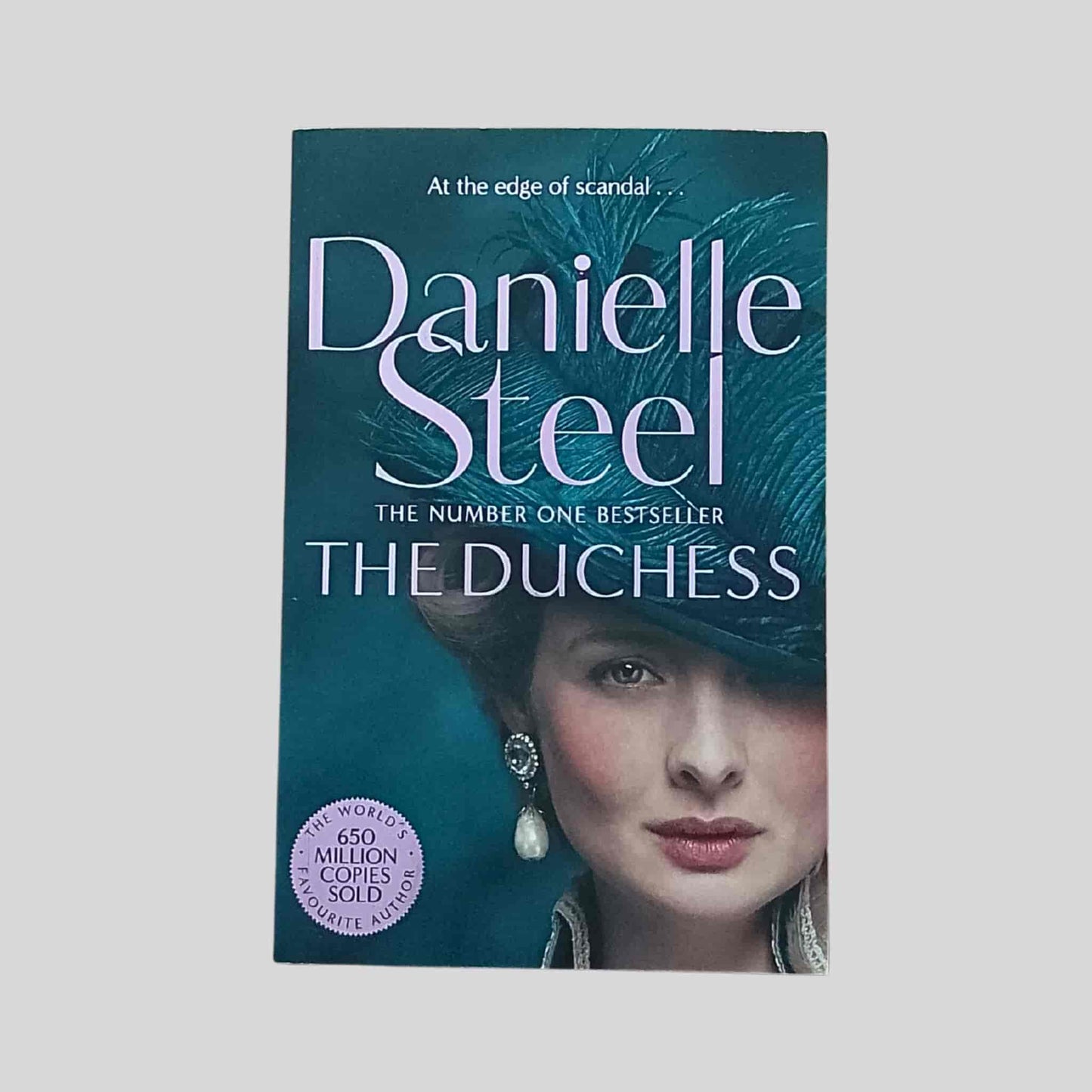 Paperback book cover of The Duchess by Danielle Steel, featuring a close-up portrait of a woman in a teal hat with feather detail, set against a dark green background