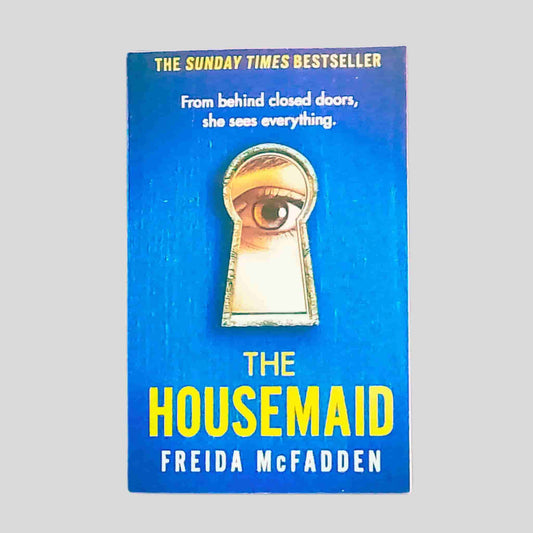 Front cover of The Housemaid by Freida McFadden – vivid blue background with a keyhole illustration showing a woman's eye