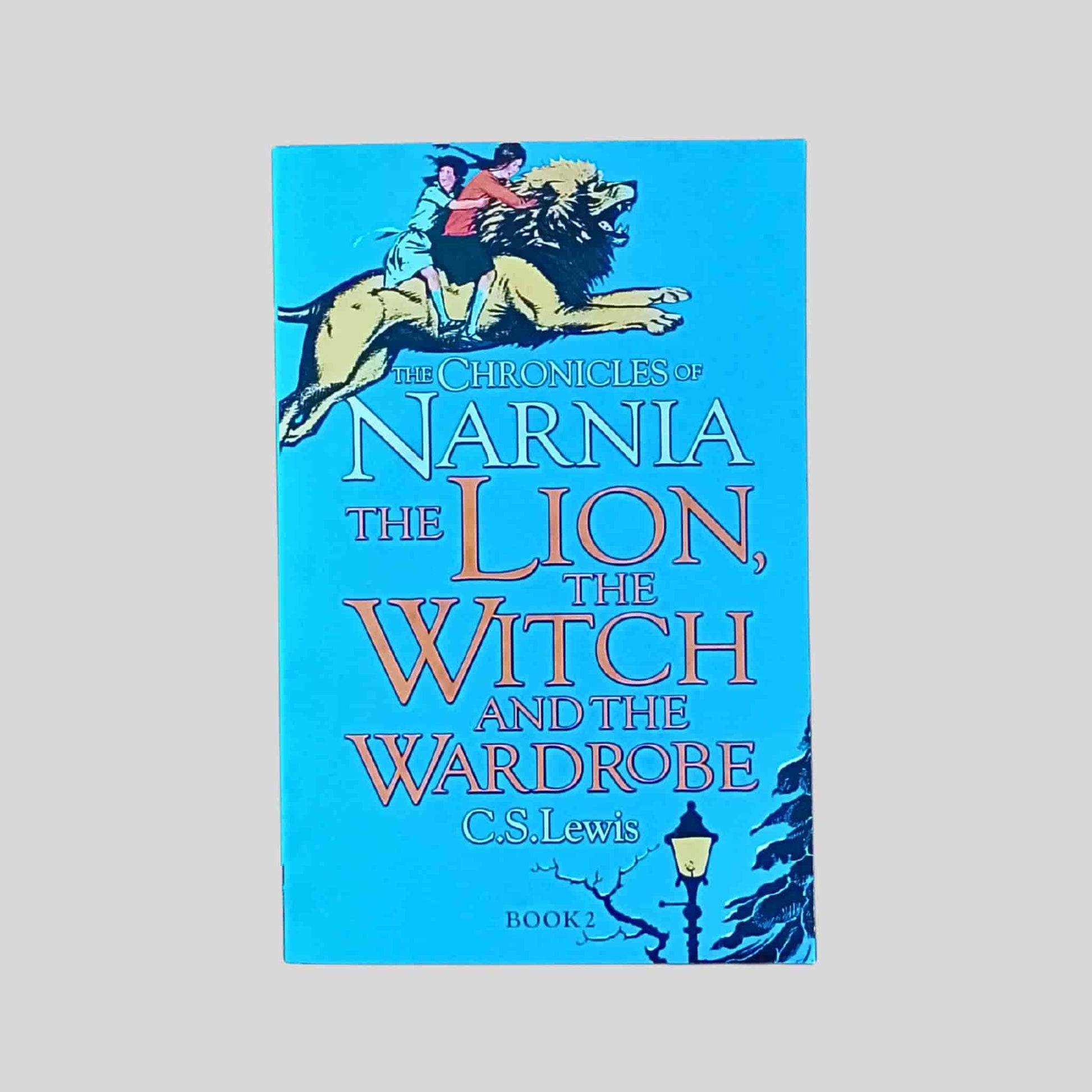 The front book cover of The Lion, the Witch and the Wardrobe by C. S. Lewis, showing two children riding on a lion against a blue background
