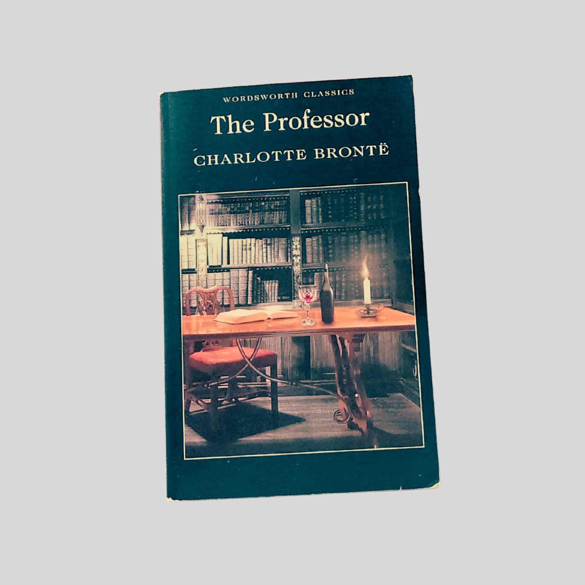 Paperback cover of The Professor by Charlotte Brontë showing a candlelit library scene with bookshelves, a wooden table, and a chair