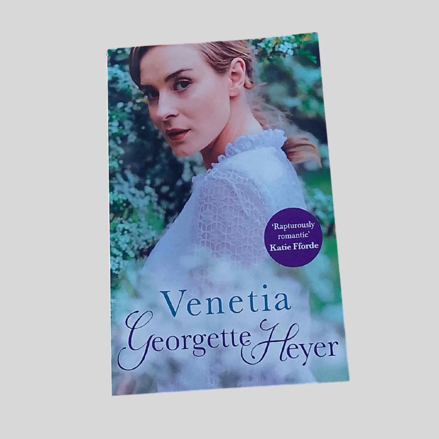 Front cover of Venetia by Georgette Heyer, paperback edition, featuring a young woman in a Regency-style white dress standing in a green garden setting